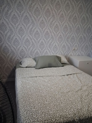 A bed with a patterned bedspread, a pillow, and a bedside table.