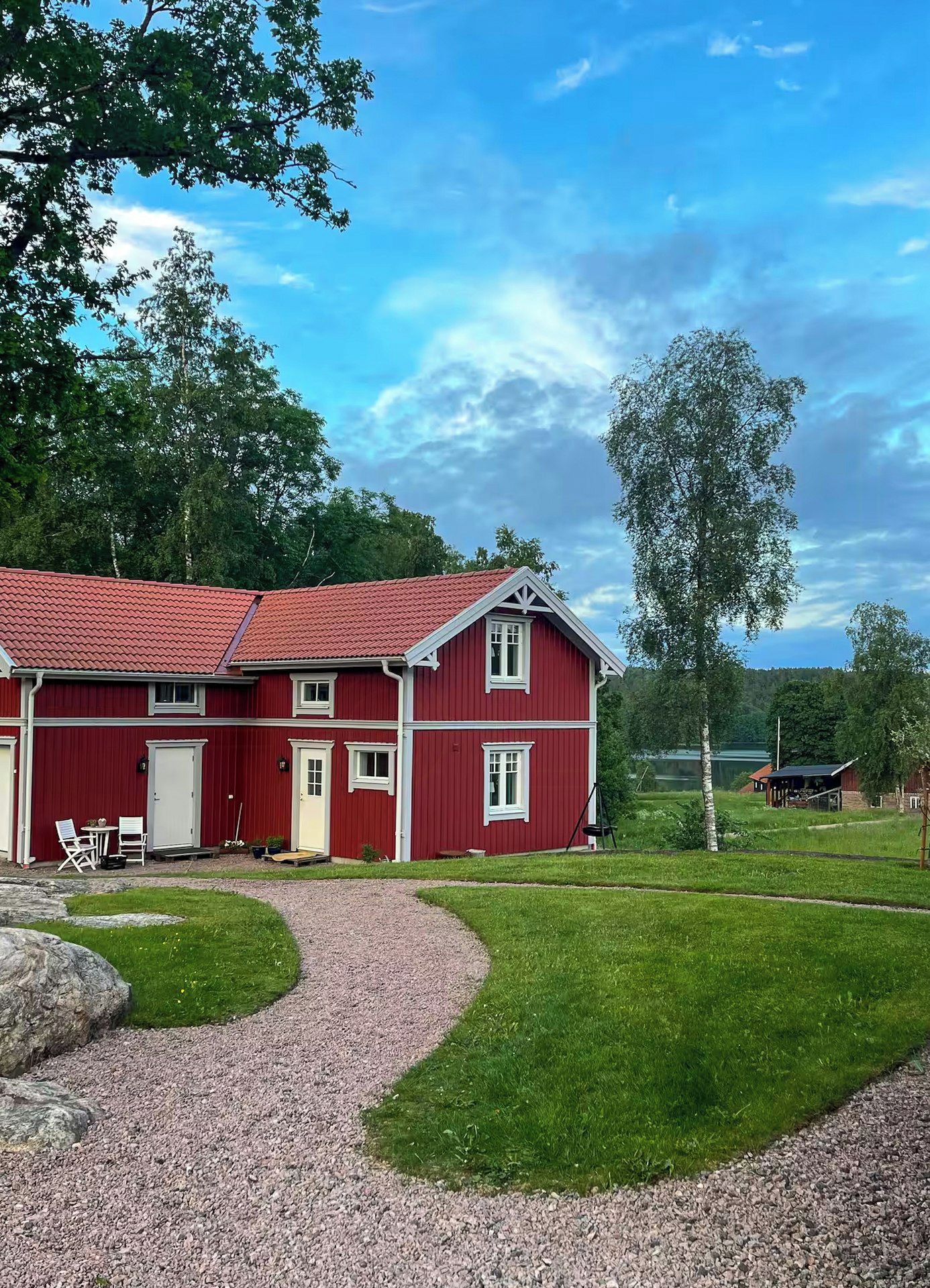 Una casa rossa a due piani con vialetto sterrato e prato.