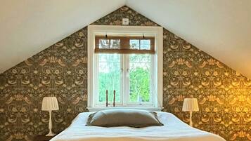A bedroom with a sloped ceiling, a bed with a white bedspread, two bedside lamps, and a wooden bench.