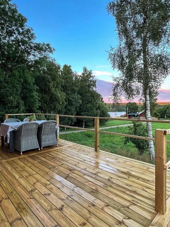 A wooden deck with wicker furniture, overlooking a grassy area and a body of water.