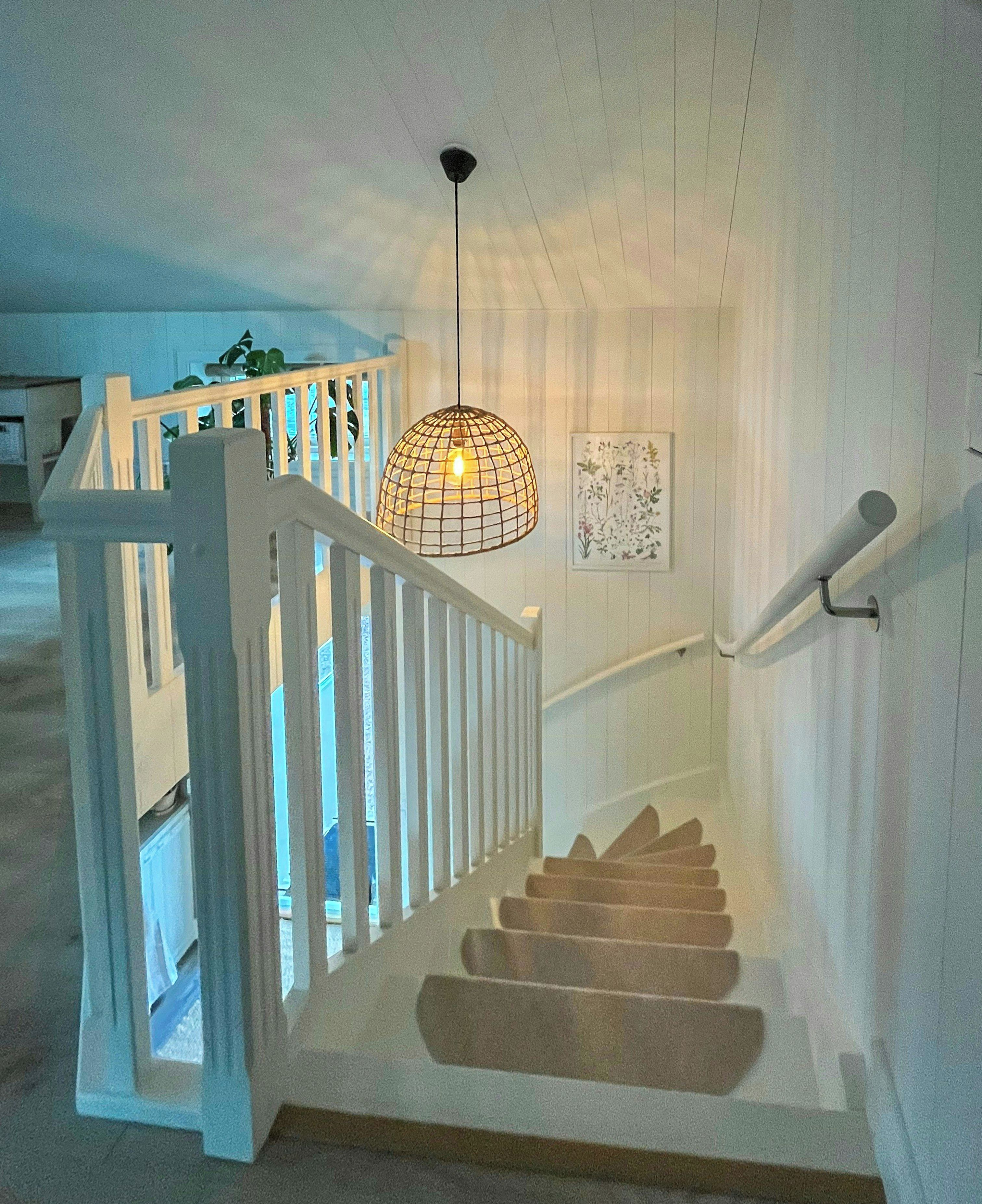 A staircase with a white railing, a hanging light fixture, and a framed picture on the wall.
