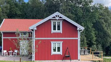 A red wooden house with a white trim, a porch with outdoor furniture, and a grassy yard.