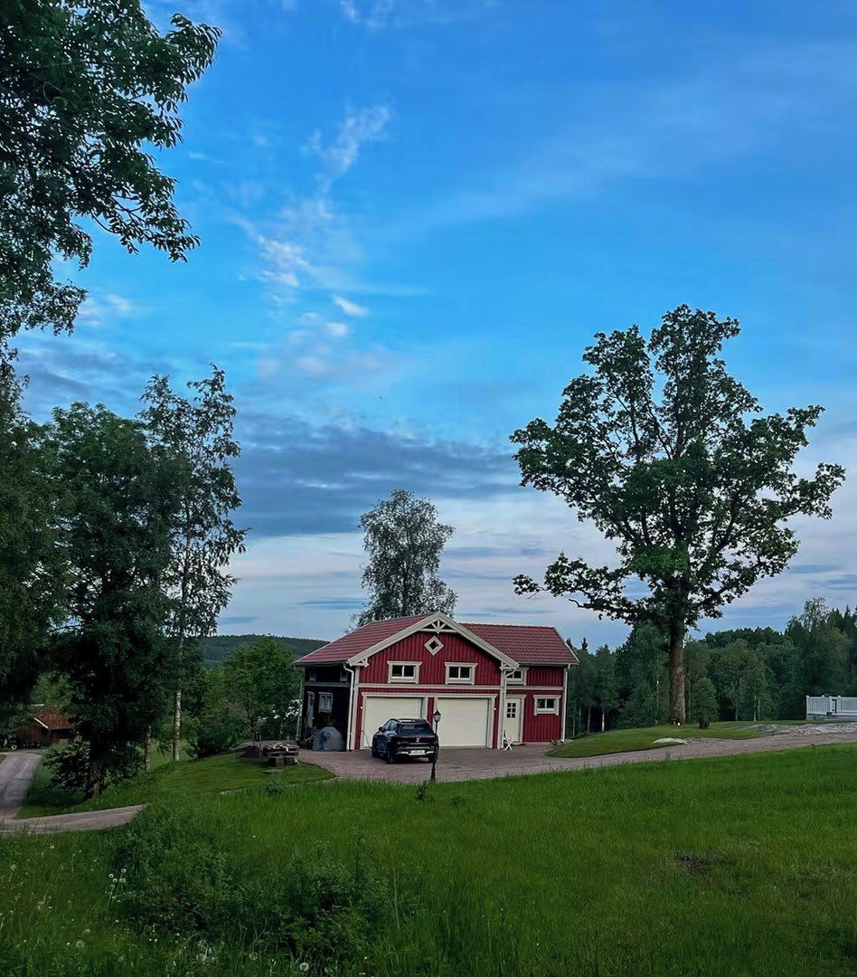 A red barn with a white garage door, surrounded by lush green fields and trees.