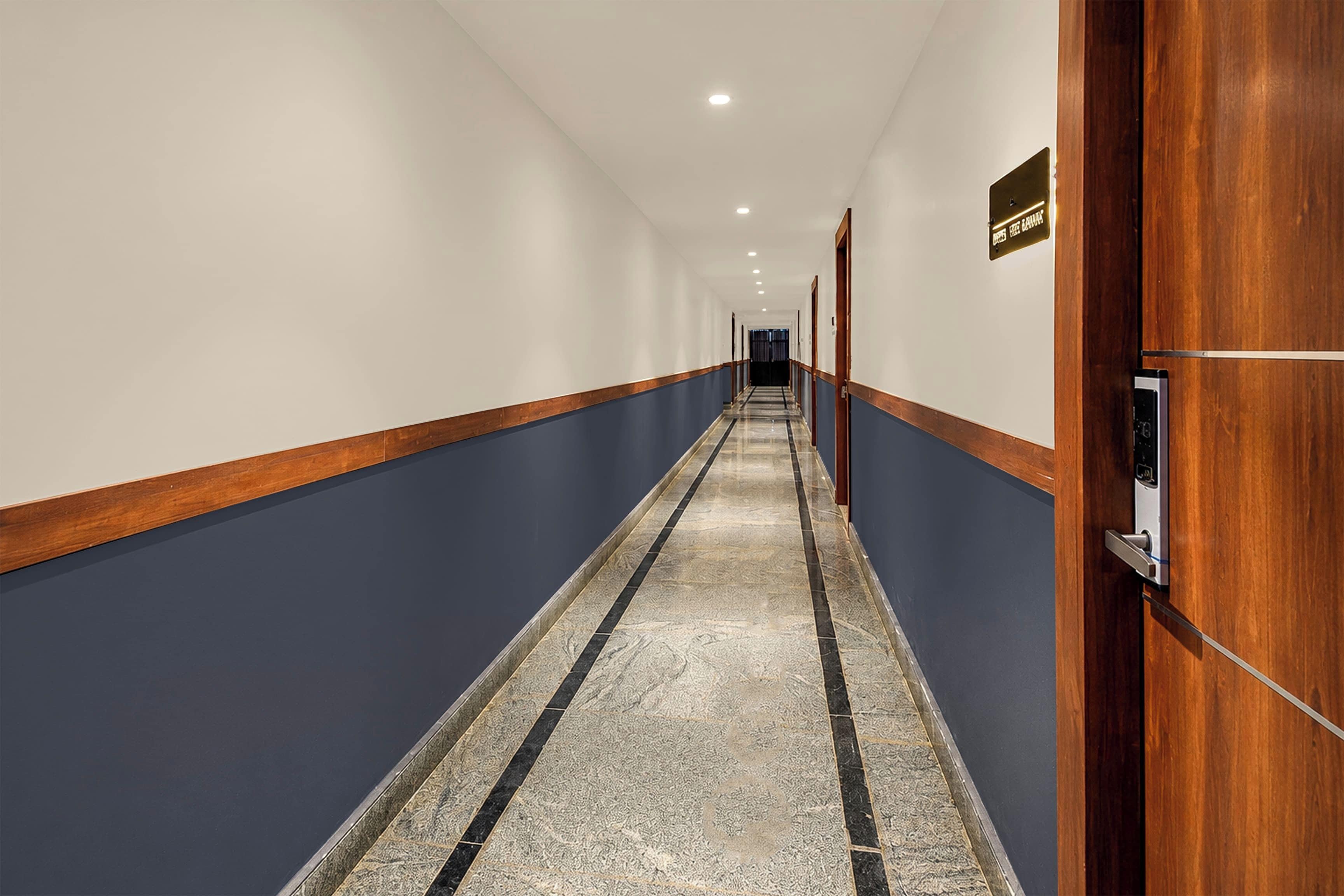 A hotel hallway with a marble floor, wooden doors, and a sign indicating the direction to the elevator.