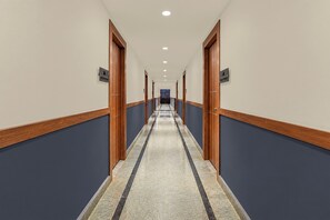 A hotel corridor with wooden doors, a tiled floor, and a blue wall.
