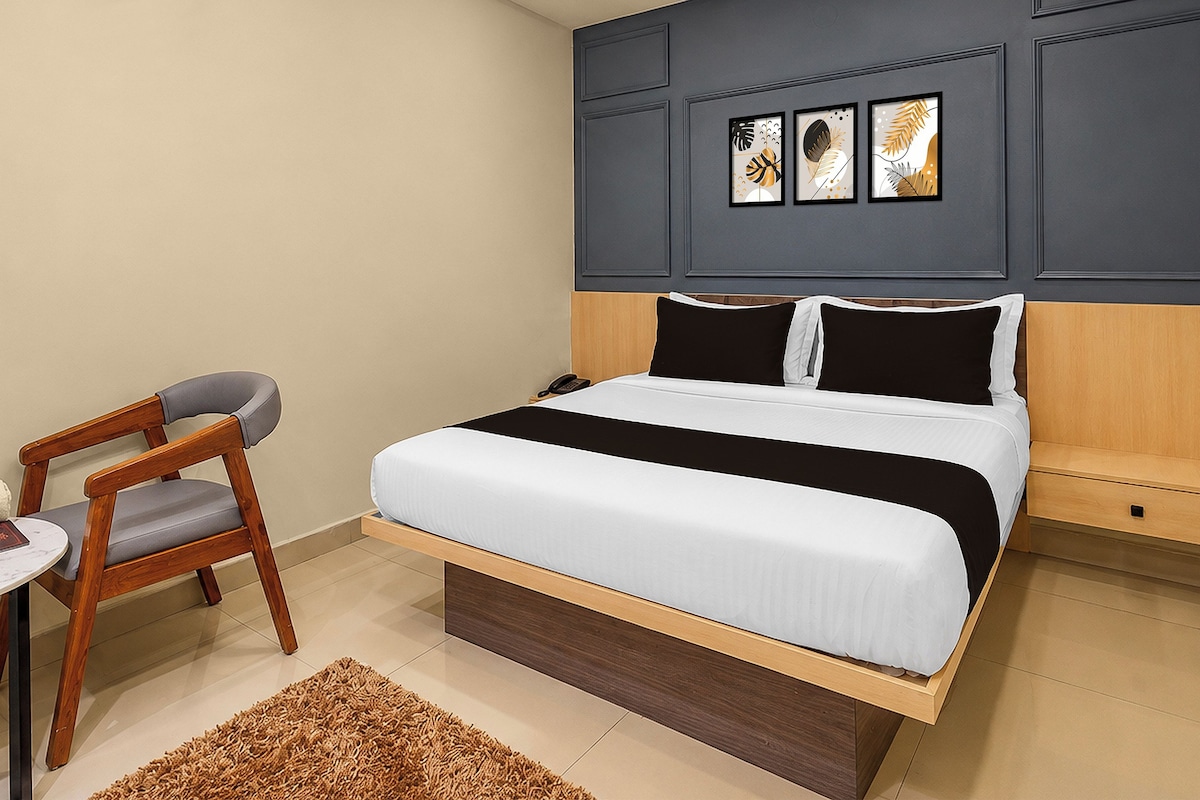 A hotel room with a bed, bedside table, chair, and a wall with framed artwork.