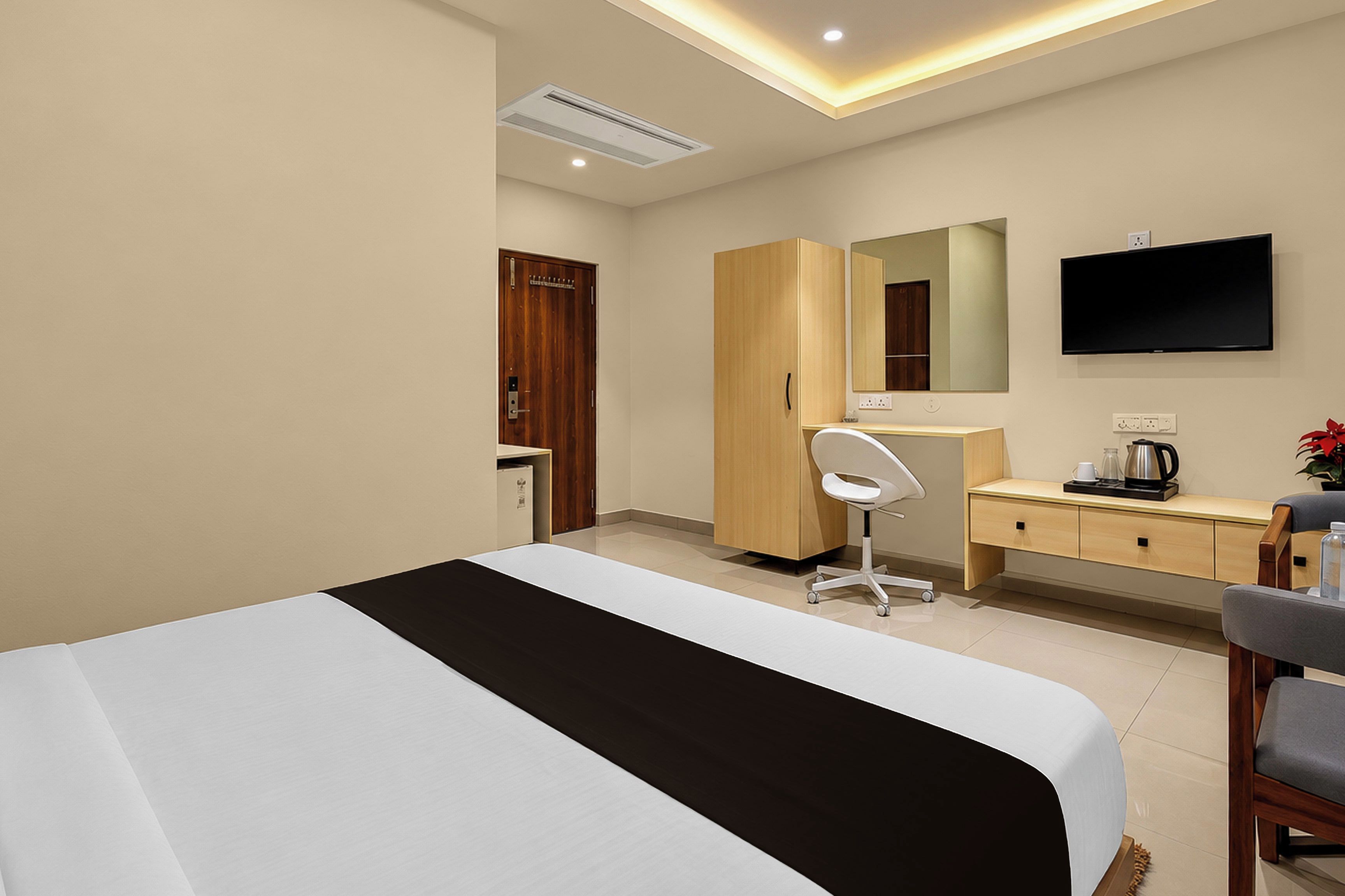 A hotel room with a bed, a desk, a chair, a television, and a mirror.