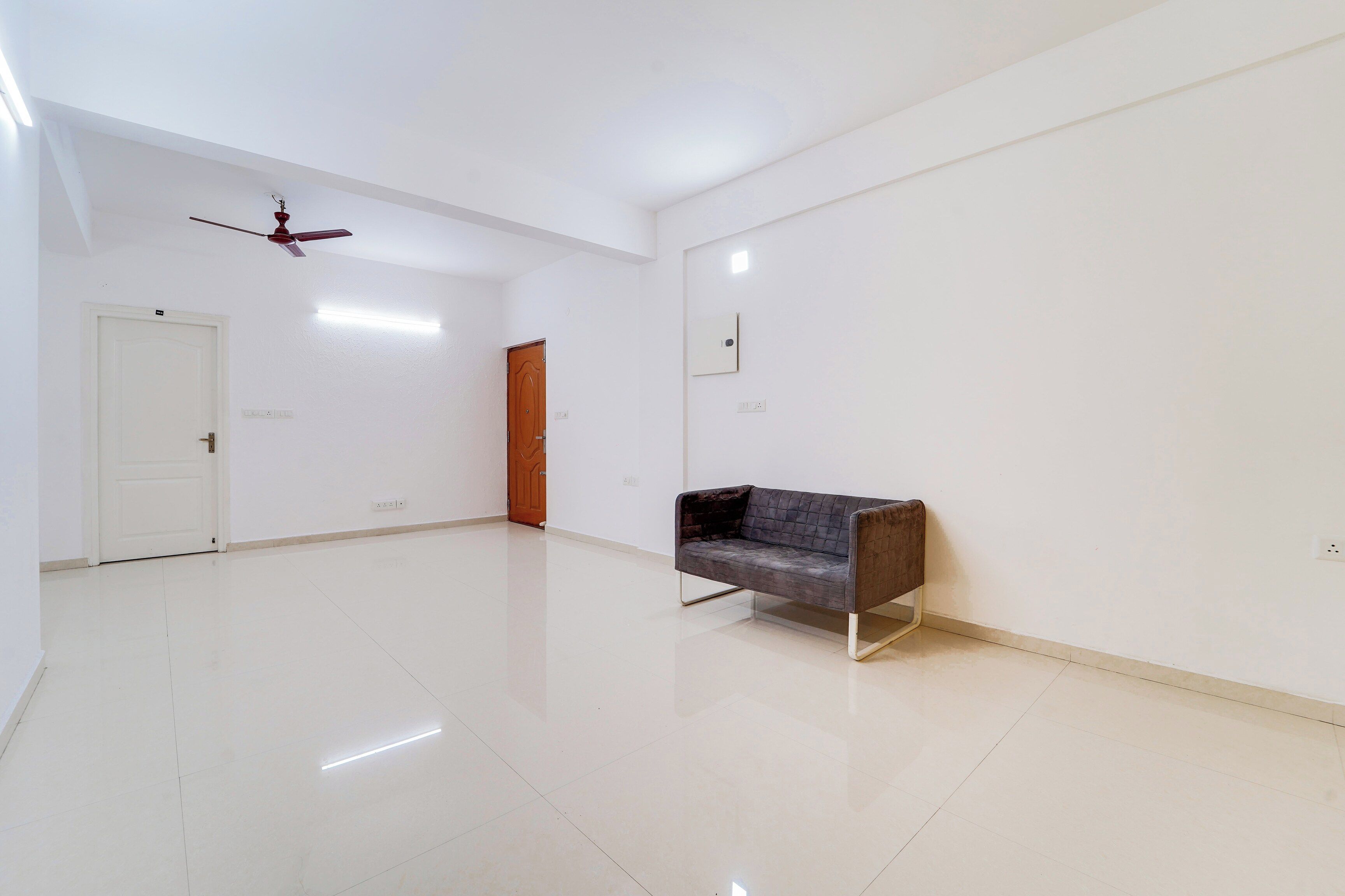 Une pièce spacieuse avec un plancher blanc, une porte en bois, un ventilateur de plafond et un canapé.