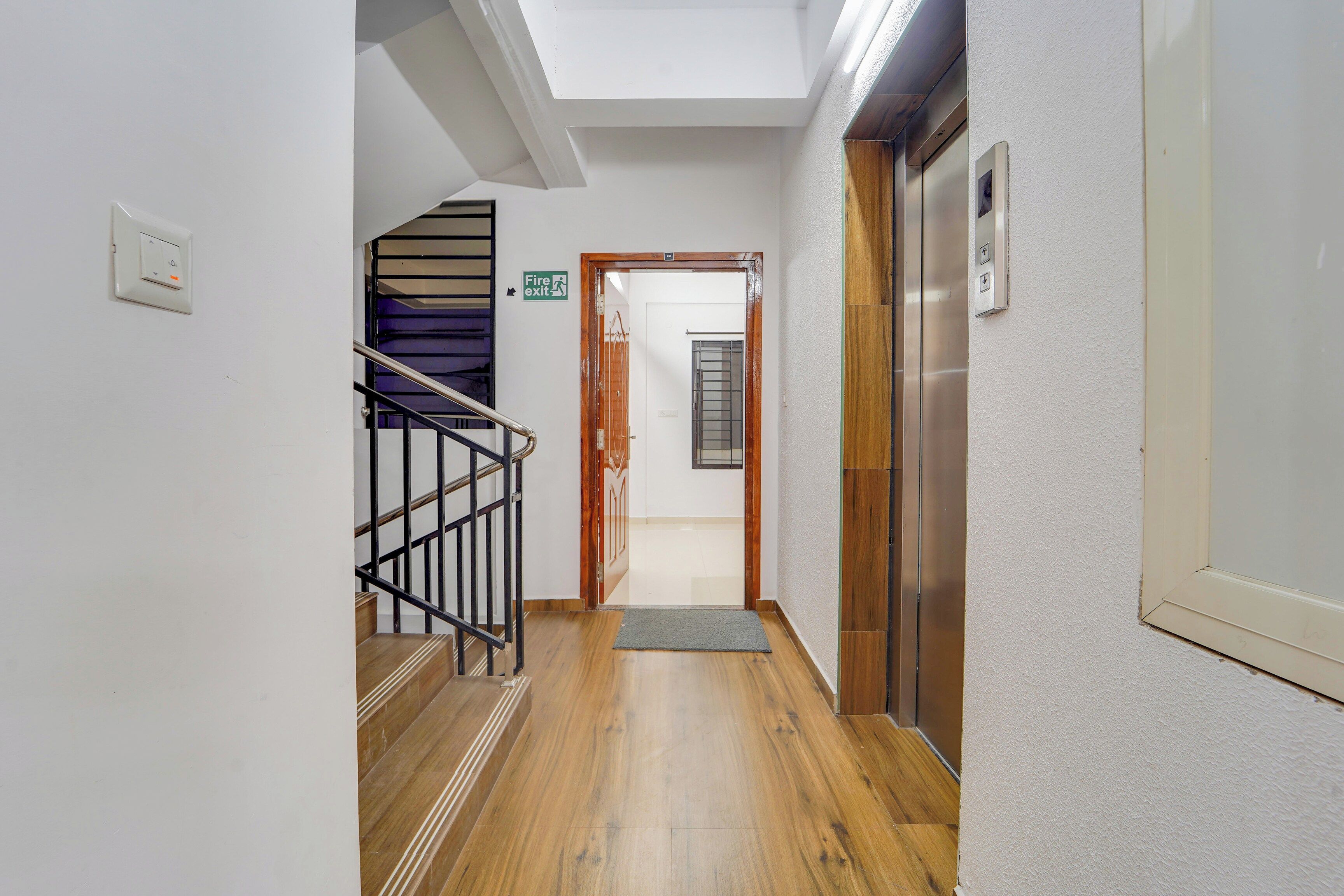 Un pasillo con piso de madera, una escalera con barandillas negras y un ascensor.