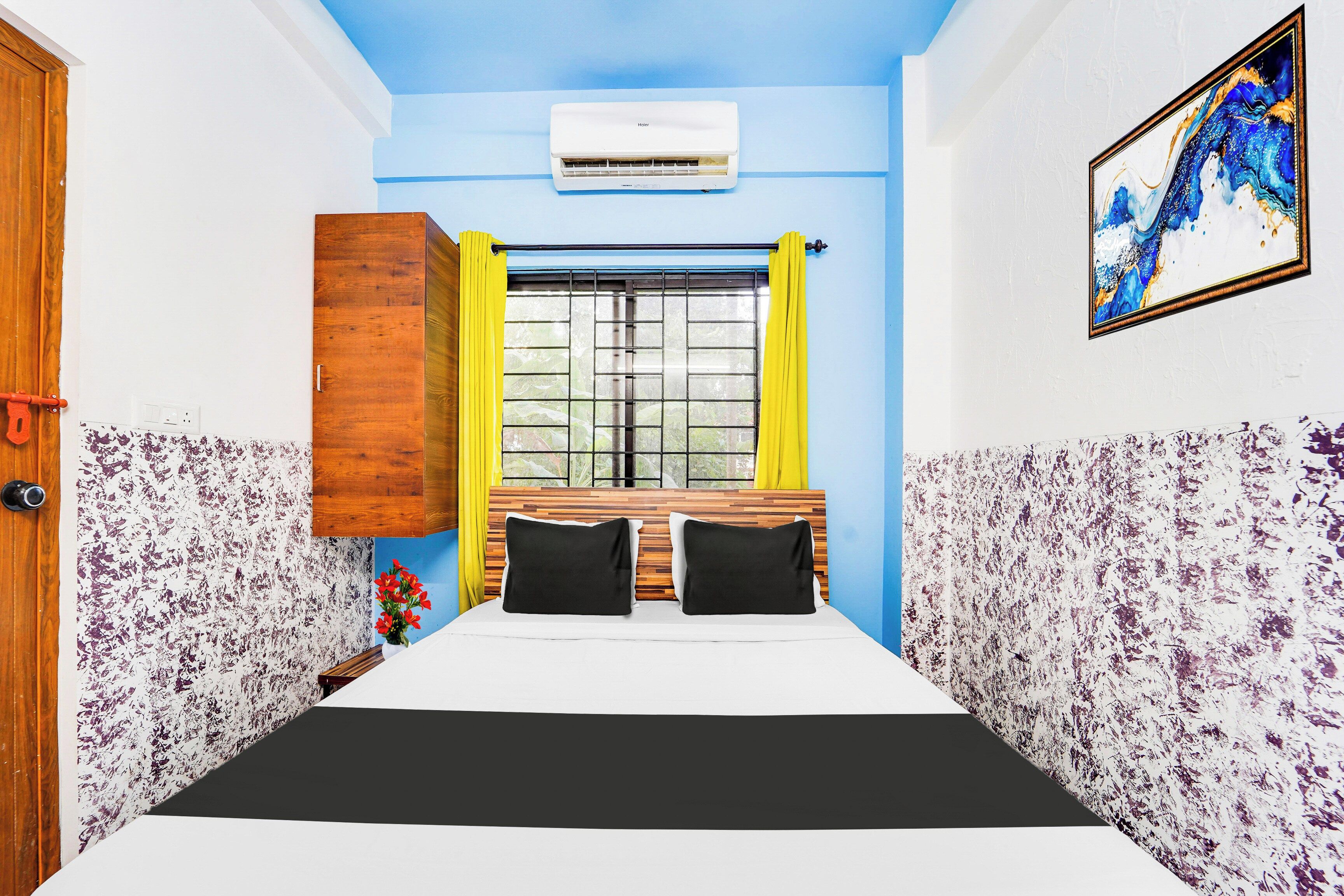 Une chambre à coucher avec un lit, une fenêtre ornée de rideaux jaunes, une tête de lit en bois et un climatiseur fixé au mur.
