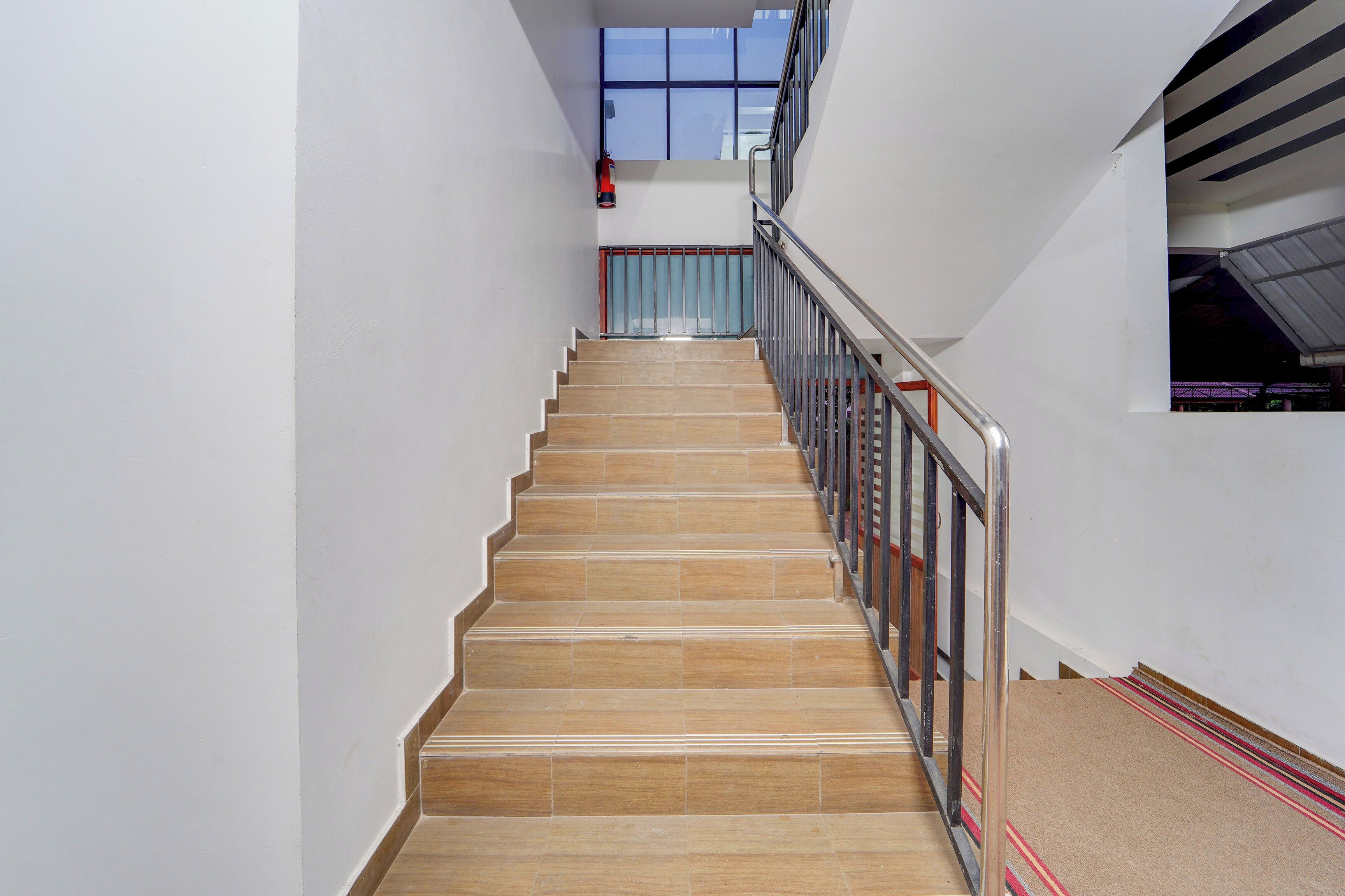 Un escalier avec une rampe en métal, menant à un palier doté d’une fenêtre.