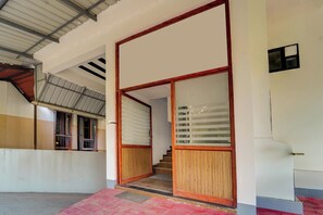 Entrada de prédio com porta de madeira, escadas e telhado de metal.