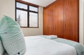 Un dormitorio con cama, ventana con persianas y armario de madera.