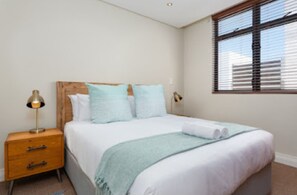 Une chambre à coucher avec un lit, une table de chevet, une lampe et une fenêtre avec des stores.