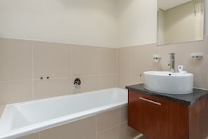 A bathroom with a bathtub, a sink, and a mirror. - Serene 1-bedroom apartment in vibrant Big Bay neighborhood (Cape Town)