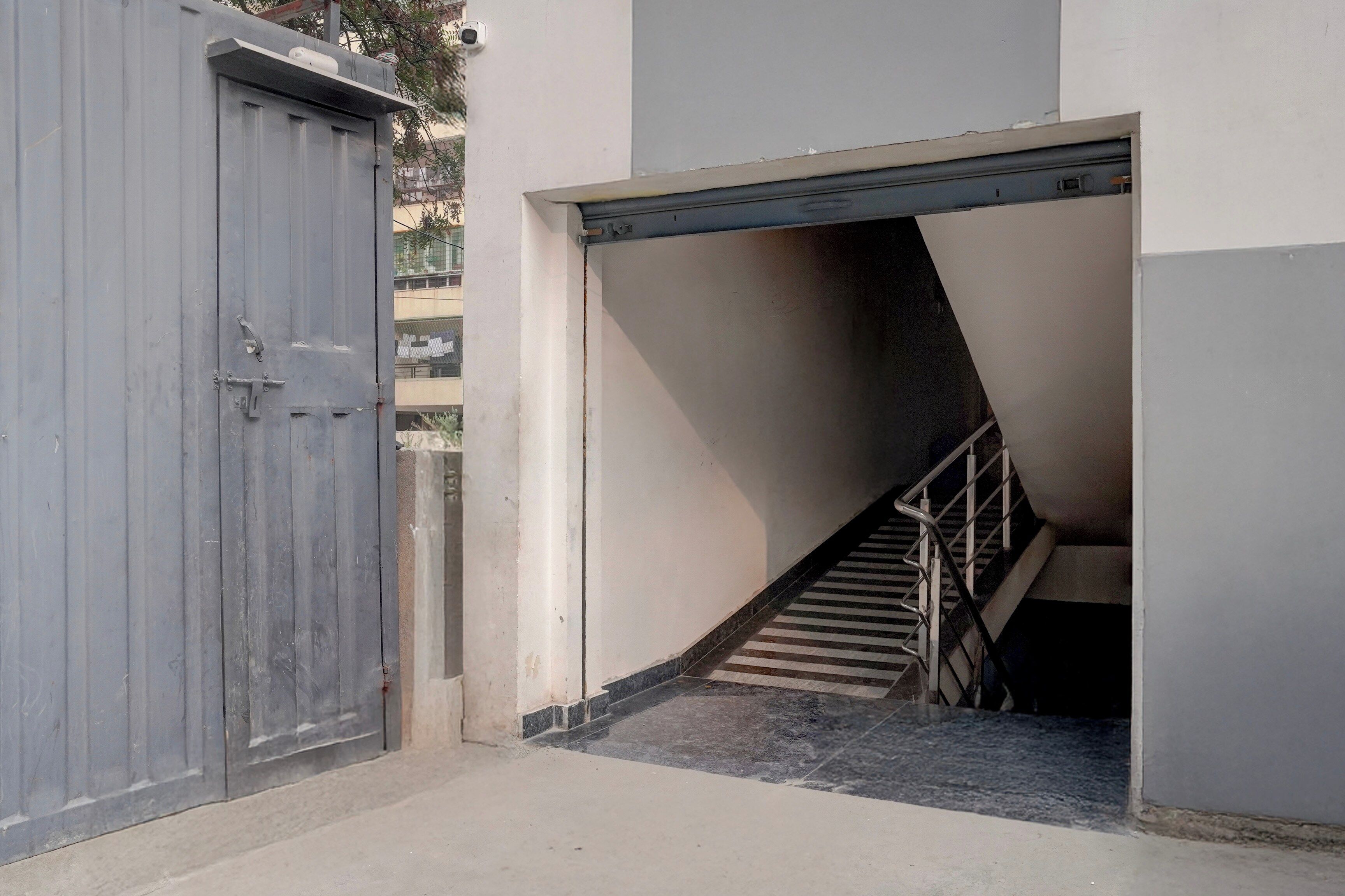 A narrow stairway leading to a garage door, with a metal handrail and a concrete floor.