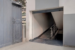 A narrow stairway leading to a garage door, with a metal handrail and a concrete floor.