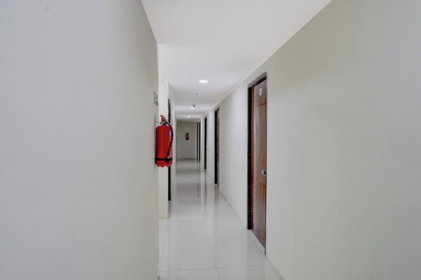 A corridor with white walls, a fire extinguisher mounted on the wall, and doors on the right side.
