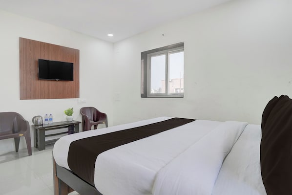 A hotel room with a bed, a desk, a chair, a television mounted on the wall, and a window.