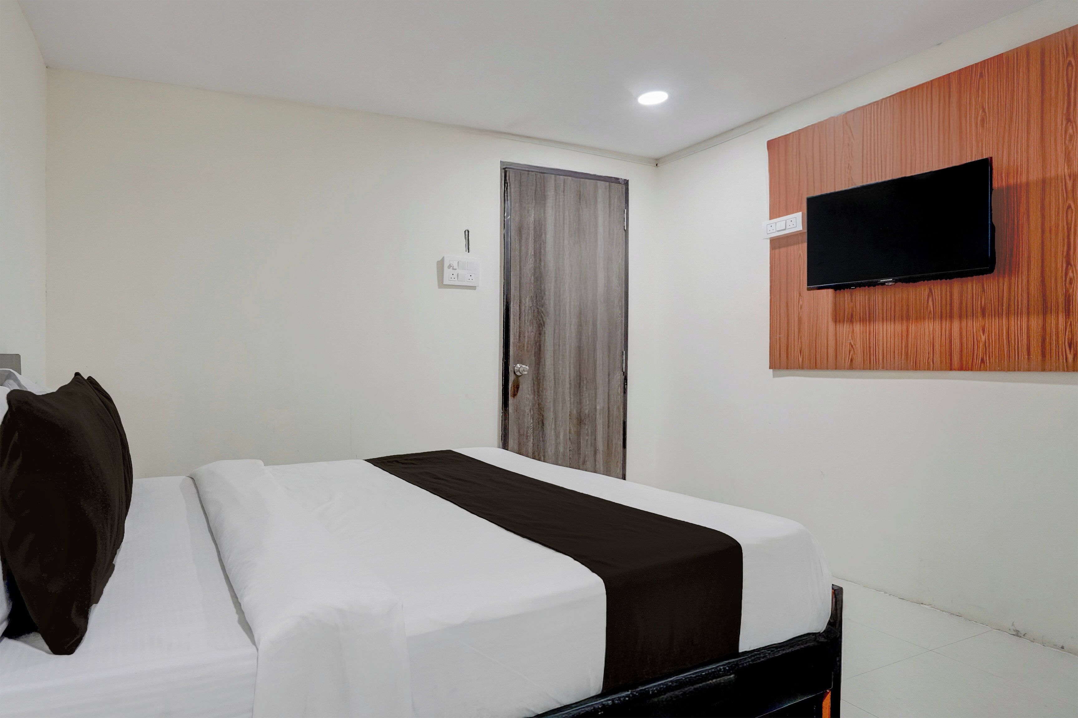 A hotel room with a bed, a television mounted on the wall, and a door.