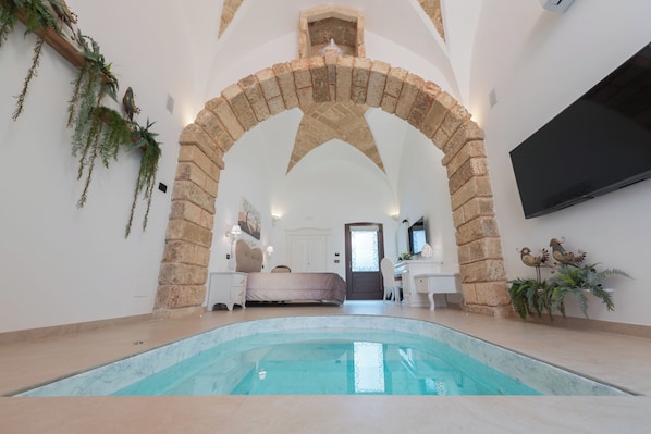 A room with a stone archway, a bed, a desk, a chair, and a television mounted on the wall.