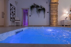 A swimming pool with a blue-lit interior, a white chair, a door leading to a purple-lit room, and decorative wall art.