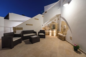 An outdoor patio with wicker furniture, a stone fireplace, and a small kitchen area.