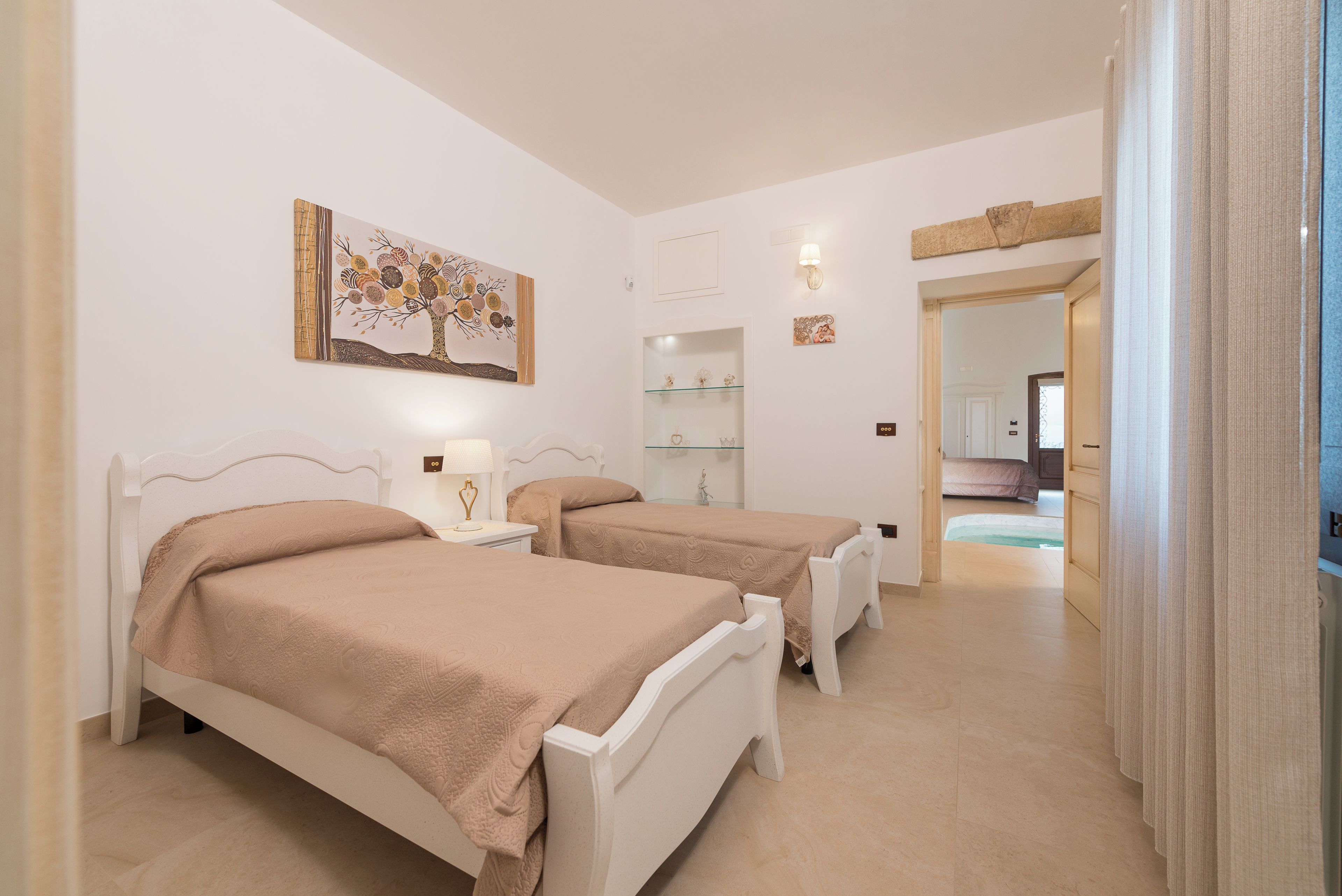 Camera d'albergo con due letti, un quadro appeso al muro, un comodino con una lampada e vista su una zona piscina.