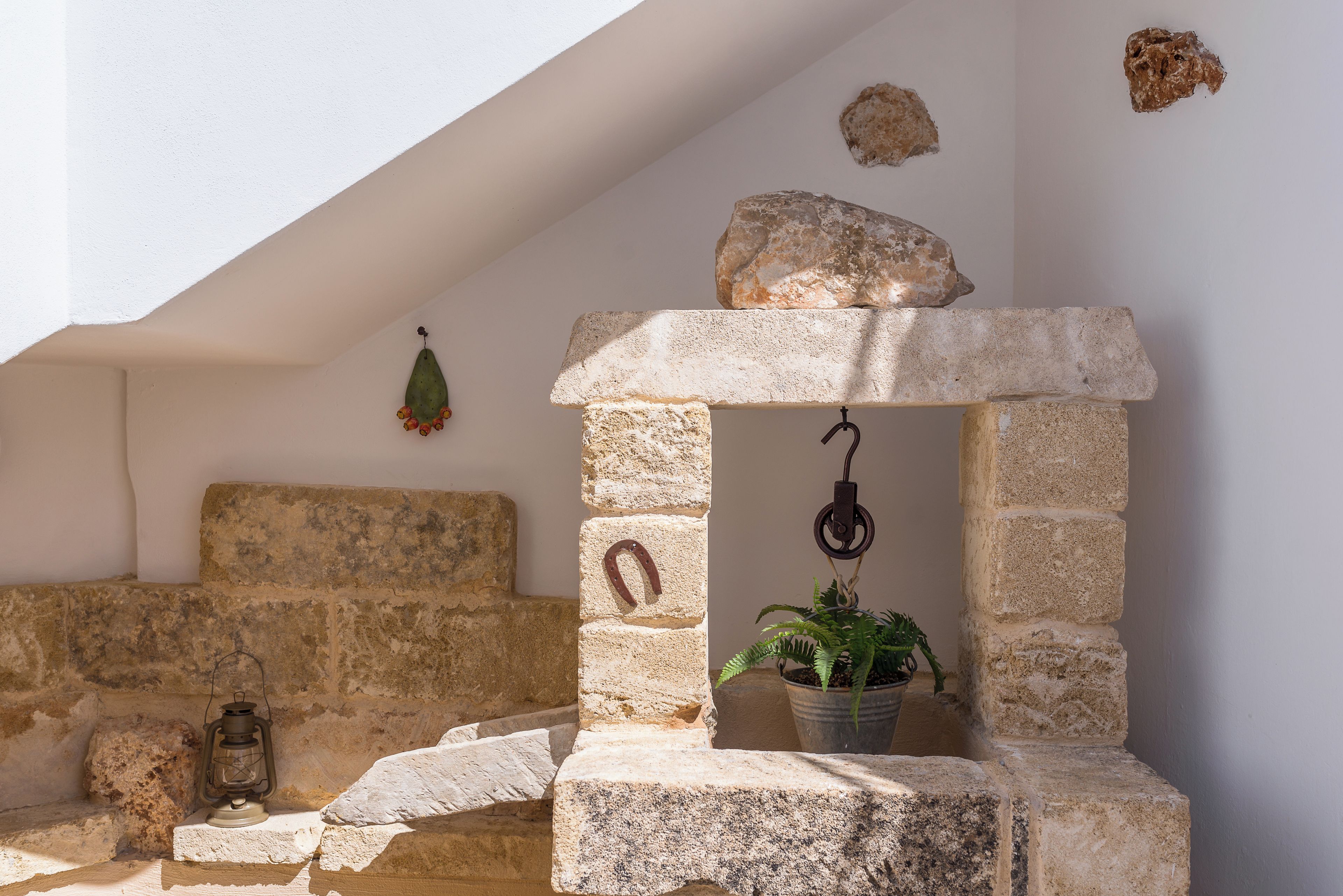 A stone bench with a lantern, a stone wall, and a hanging plant.