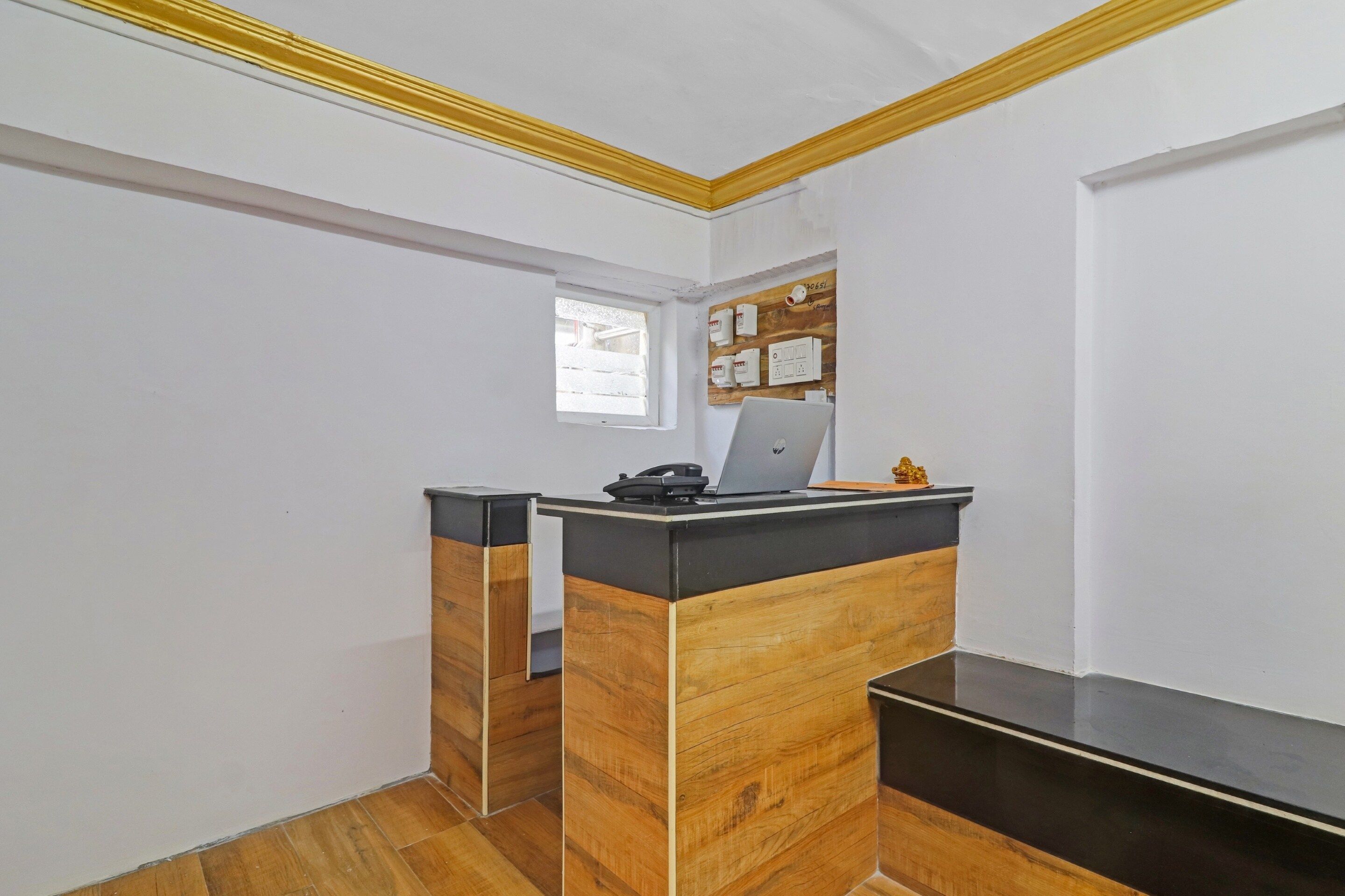 Un mostrador de recepción con detalles de madera, una pequeña ventana y un panel eléctrico instalado en la pared.
