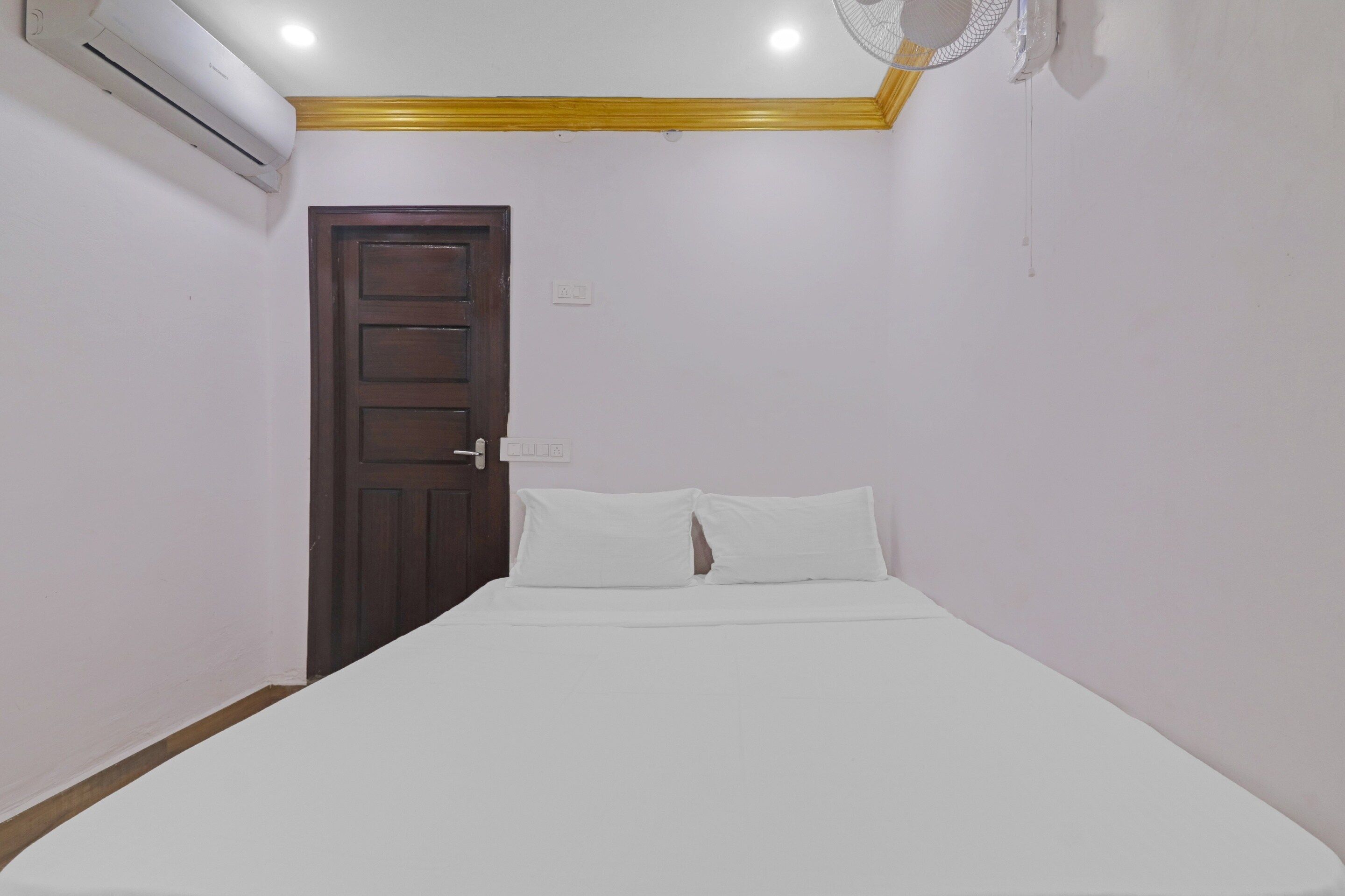 Una habitación pequeña con cama individual, puerta de madera y colcha blanca.