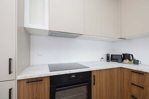 Modern kitchenette with white cabinets, wood-effect lower cupboards, built-in oven and a spacious countertop. - Comfortable Apartment in Warsaw with Workspace by Noclegi Renters (Warszawa)