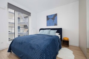 A bedroom with a bed, a window, a painting, and a small wooden nightstand. - Comfortable Apartment in Warsaw with Workspace by Noclegi Renters (Warszawa)
