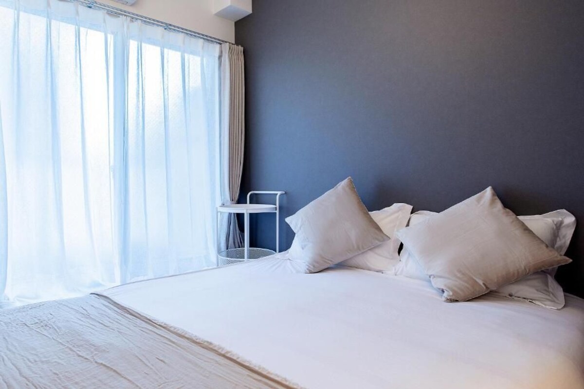 A hotel room with a bed, white bedding, a side table, and a window with curtains.