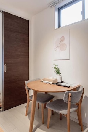 A dining area with a wooden table and four chairs, a framed picture on the wall, and a window above the table. - Tabi Time Gangtian Imazato (Osaka, Ikuno-ku)