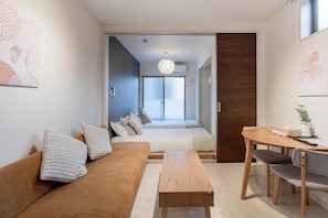 A modern living room with a sofa, a wooden coffee table, and a dining area with a table and chairs. - Tabi Time Gangtian Imazato (Osaka, Ikuno-ku)