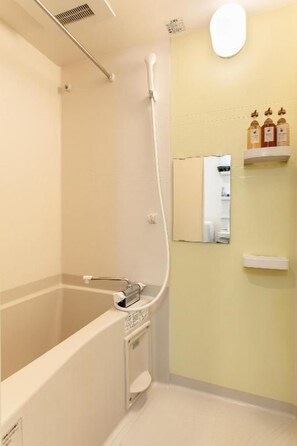 A bathroom with a bathtub, a shower, and a mirror. There are toiletries on a shelf. - Tabi Time Gangtian Imazato (Osaka, Ikuno-ku)