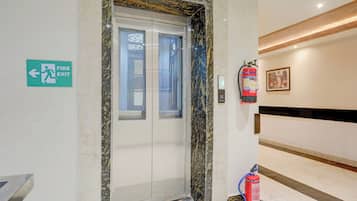 A fire exit sign, a fire extinguisher, and a marble elevator door.