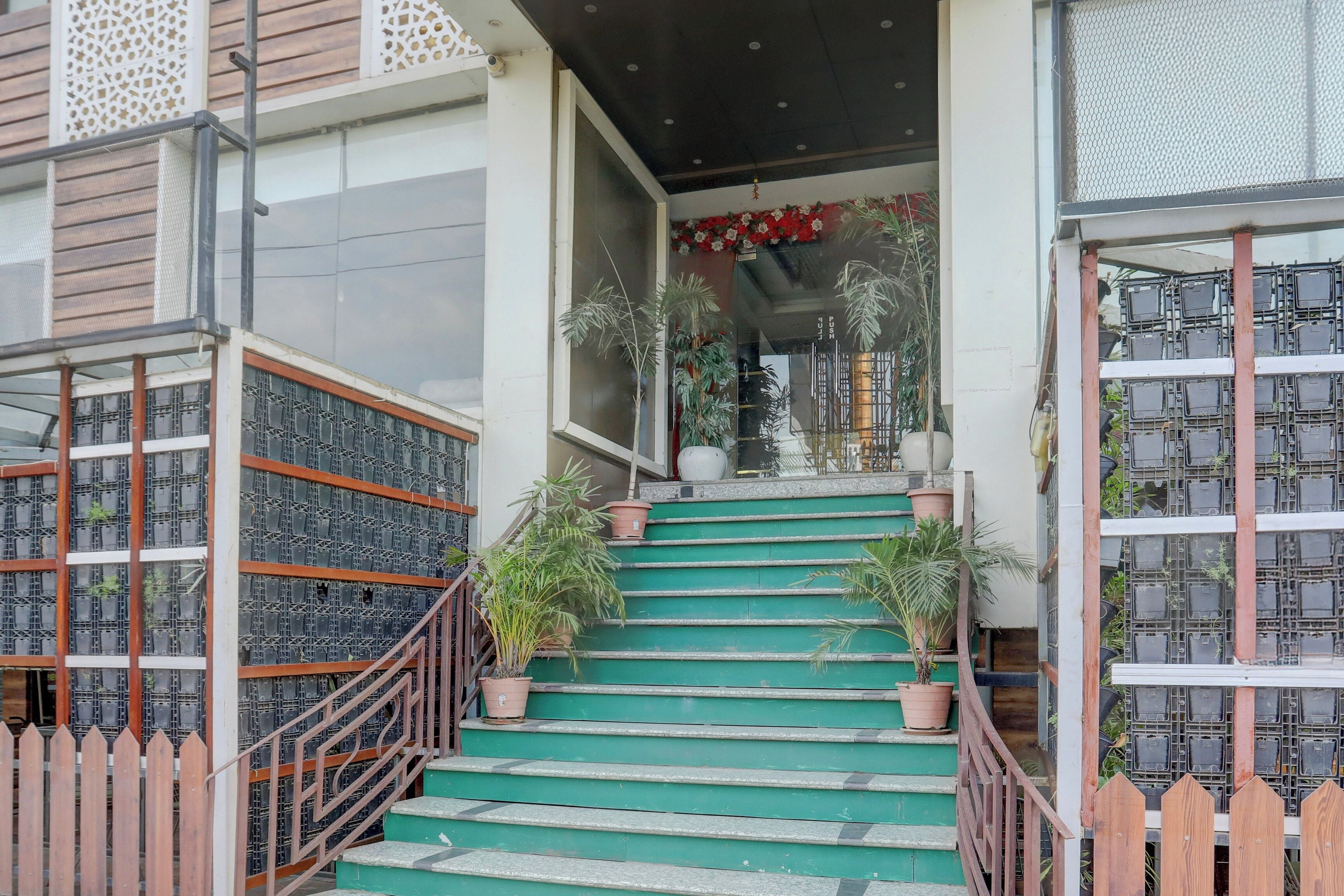 Una escalera conduce a la entrada de un edificio, con barandilla de metal y plantas en macetas.
