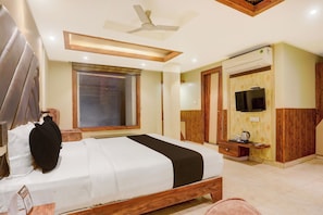 Quarto de hotel com cama, televisão, ventoinha no teto e janela com vista.