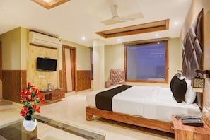 Quarto de hotel com cama, escrivaninha, cadeira, televisão e janela.