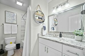 A bathroom with a toilet, sink, mirror, towel rack, and a shower curtain. - Roomy and Modern Apartment | Near AT&T Stadium (Arlington)