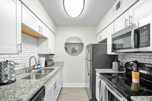 Une cuisine compacte avec des meubles blancs, un réfrigérateur en acier inoxydable, un four à micro-ondes, une cuisinière et un évier doté d’un robinet moderne.