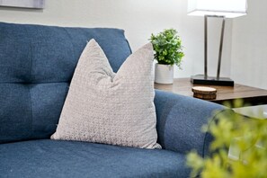 Un canapé bleu agrémenté d’un coussin texturé et d’une petite plante en pot, posés sur une table d’appoint en bois.