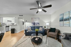 A modern living room with a ceiling fan, a sofa, a coffee table, and a view of the kitchen. - Roomy and Modern Apartment | Near AT&T Stadium (Arlington)