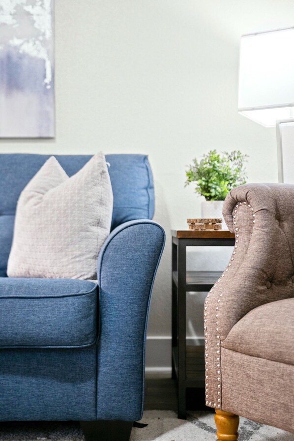 Un sofá azul con un cojín, una mesita con una planta y un sillón marrón con base de madera.