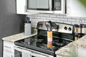 A kitchen with a stove, microwave, and various utensils. - Roomy and Modern Apartment | Near AT&T Stadium (Arlington)