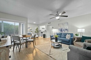 Una sala moderna con un sofá azul, sillones grises, una mesa de centro y un comedor con una mesa y sillas de madera.