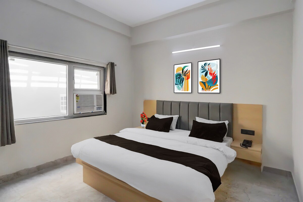 A modern hotel room with a large bed, a bedside table with a phone, and two abstract paintings on the wall.