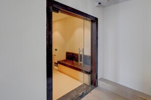 A room with a glass door leading to a seating area with a bench and a small table. - Townhouse Maha Mrityunjay Temple (Varanasi)